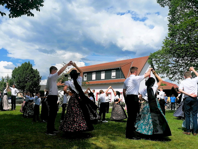 Jugendliche und Kinder in traditioneller Kleidung der sorbischen katholischen Festtagstracht tanzen im Kreis um den Maibaum.